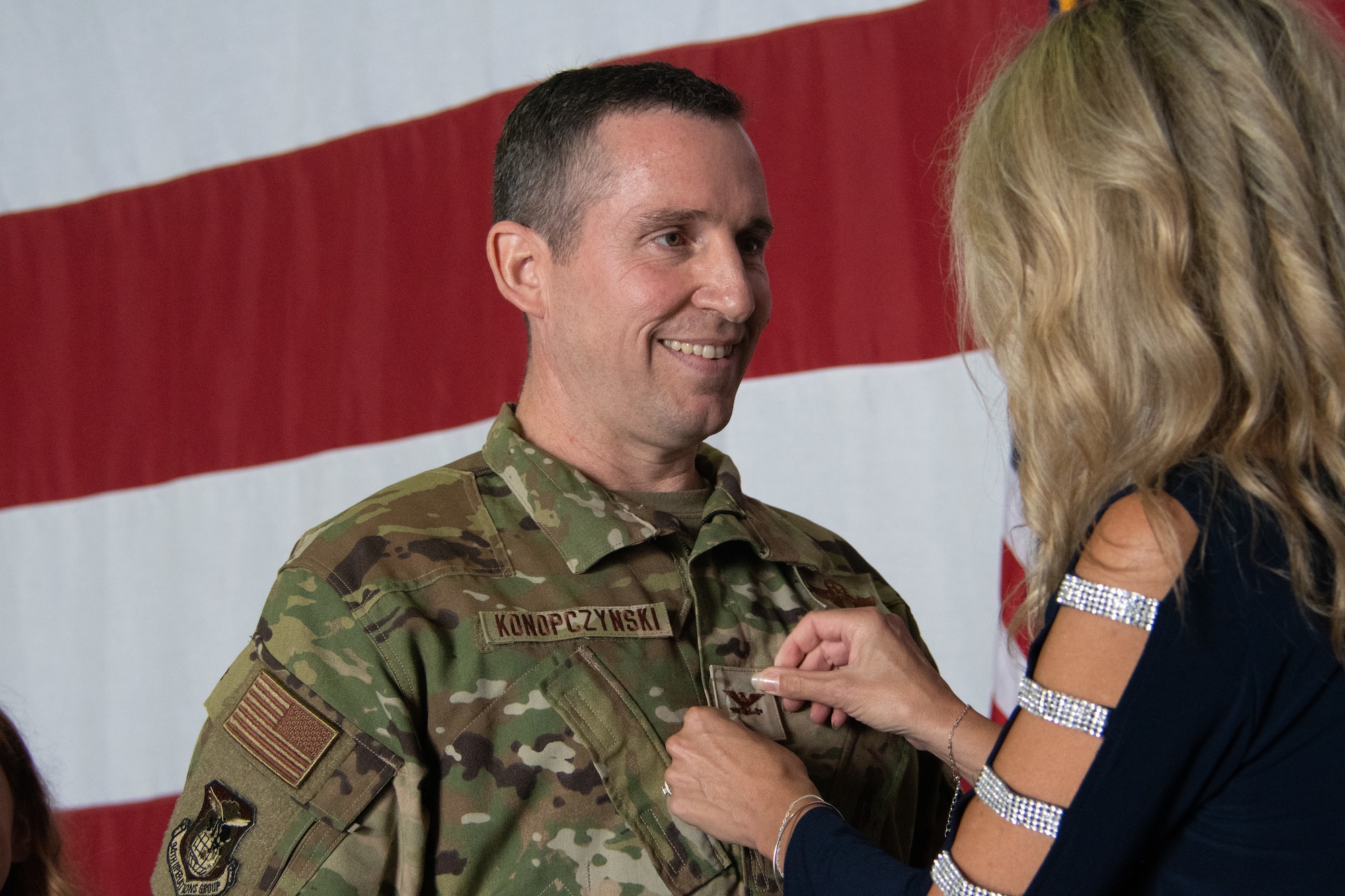 A man stands center frame and a rank is placed on his uniform
