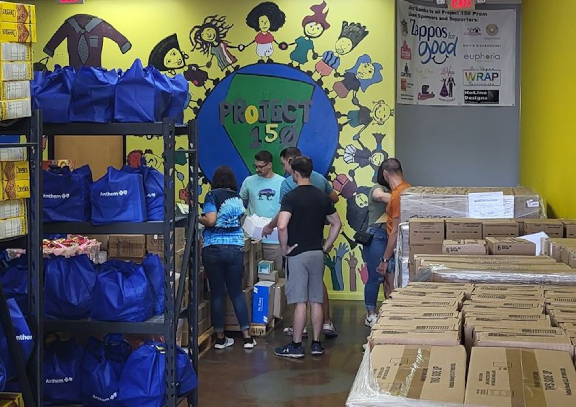 Airmen surround a table holding school supplies. Bags and boxes of donations are organized on tables and shelves.