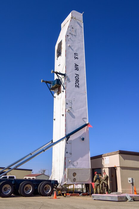 Three men stand next to a very tall missile tower.