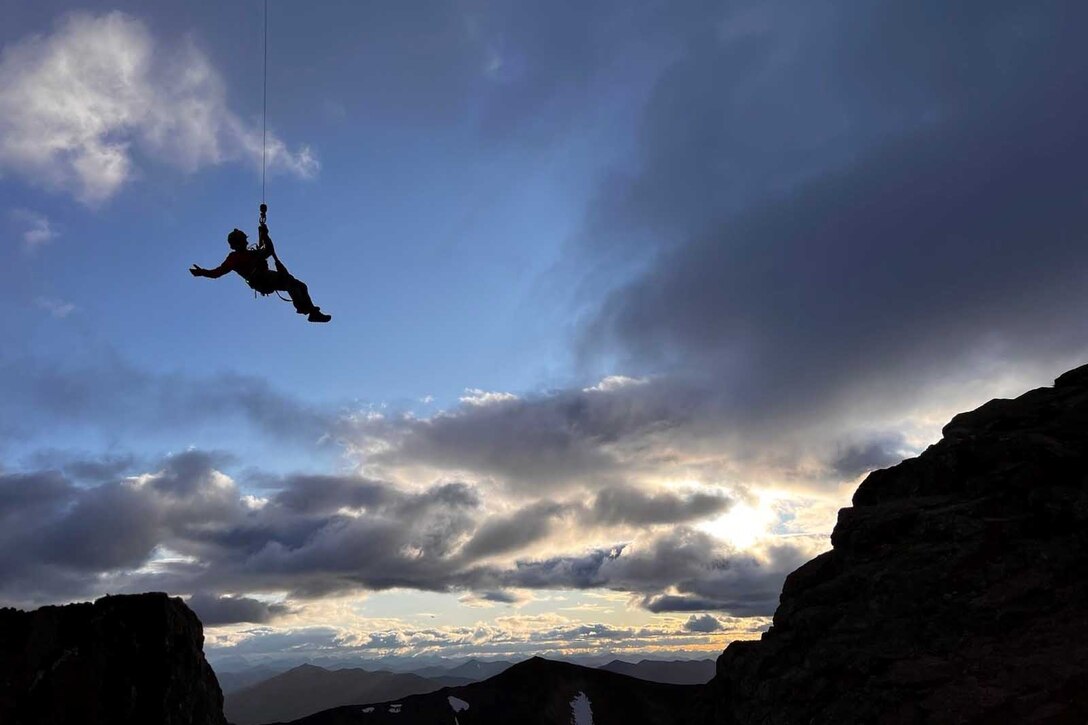 An airman hangs from a cable at twilight.