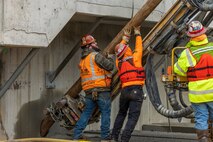 Workers help guide a hydraulic anchor drilling rig, February 16, 2023, as part of the seismic mitigation effort at Puget Sound Naval Shipyard & Intermediate Maintenance Facility.(U.S. Navy Photo by Wendy M Hallmark)