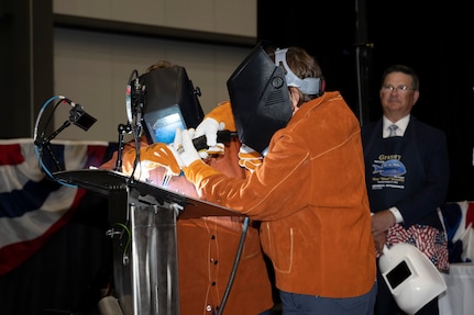 Ship Sponsor Mimi Donnelly (right) starts the welding of her initials onto the ceremonial plate that will be installed on the hull of the completed submarine with the help of Electric Boat welder Allison Fasulo. August 17, 2023.