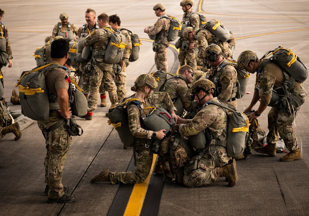 Airmen sit on the flight line checking the gear of their wingmen before loading a plane.