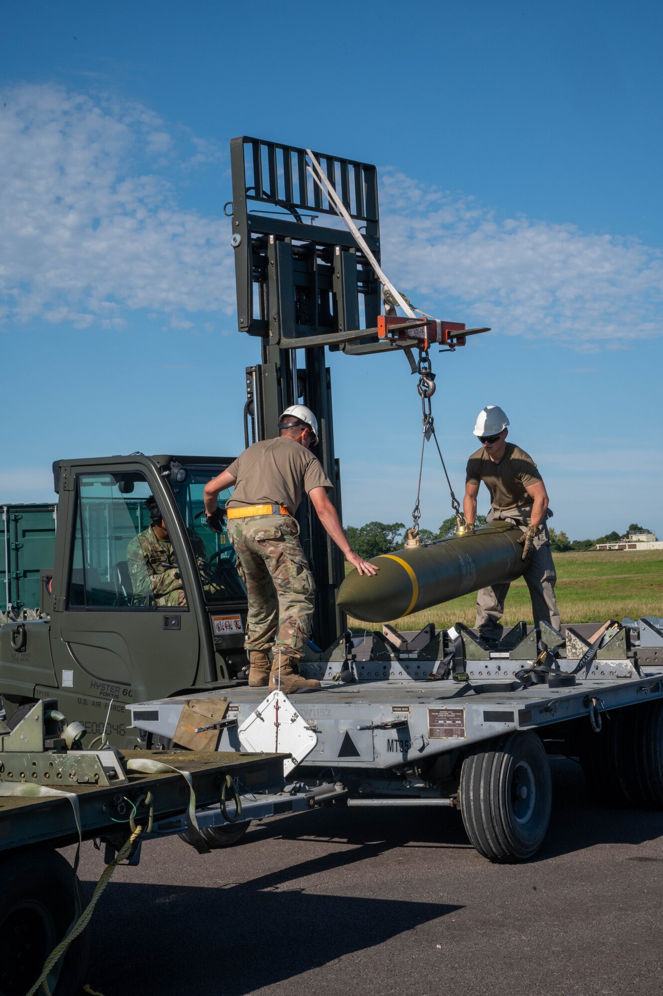 2 airmen guide a munition being listed from the trailer with a forklift.