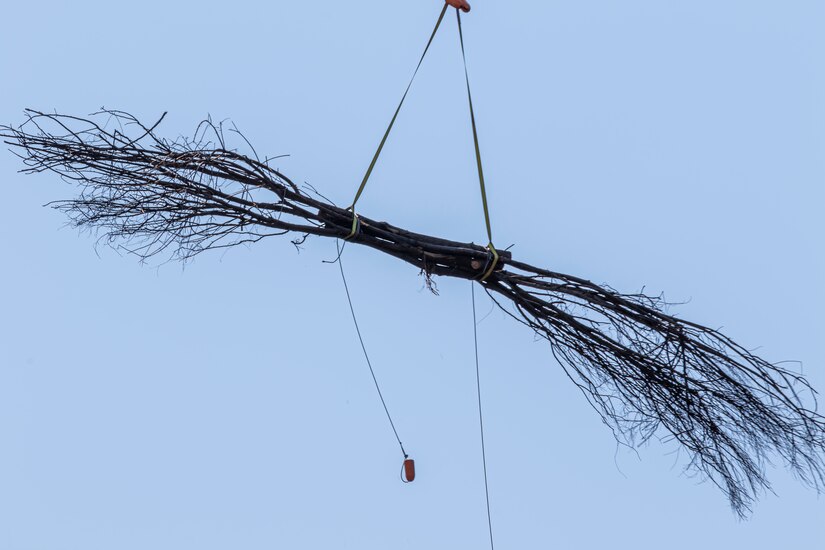 A helicopter lifting trees and concrete blocks to place them in a water basin on the Ohio River.