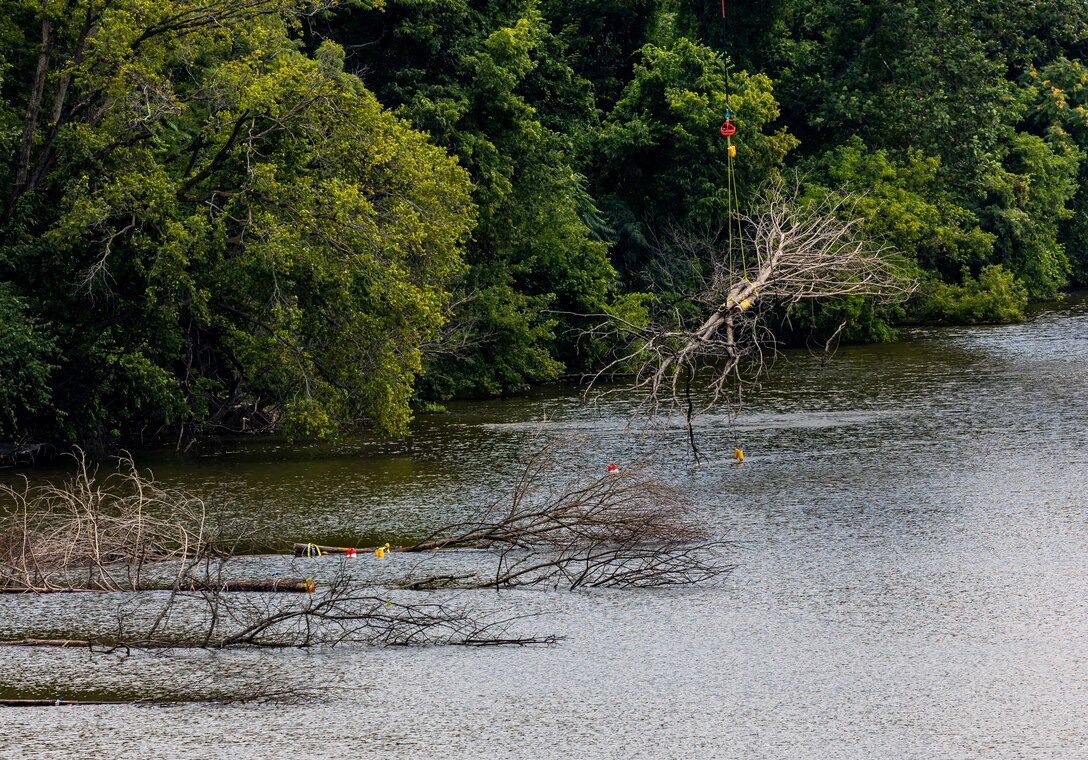 A helicopter lifting trees and concrete blocks to place them in a water basin on the Ohio River.