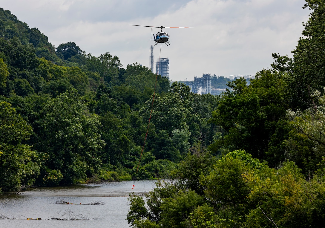 A helicopter lifting trees and concrete blocks to place them in a water basin on the Ohio River.