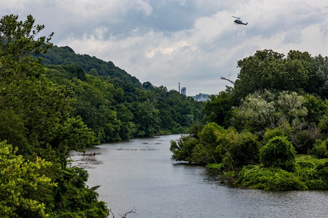 A helicopter lifting trees and concrete blocks to place them in a water basin on the Ohio River.