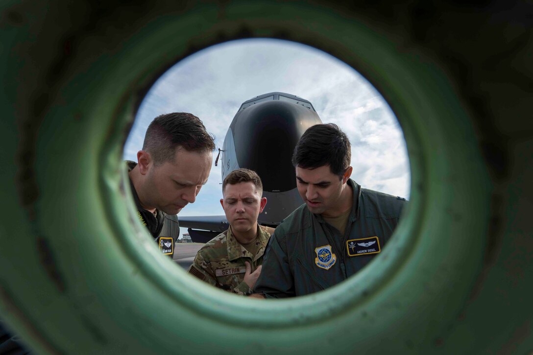 Three airmen seen through a circular opening looking down.