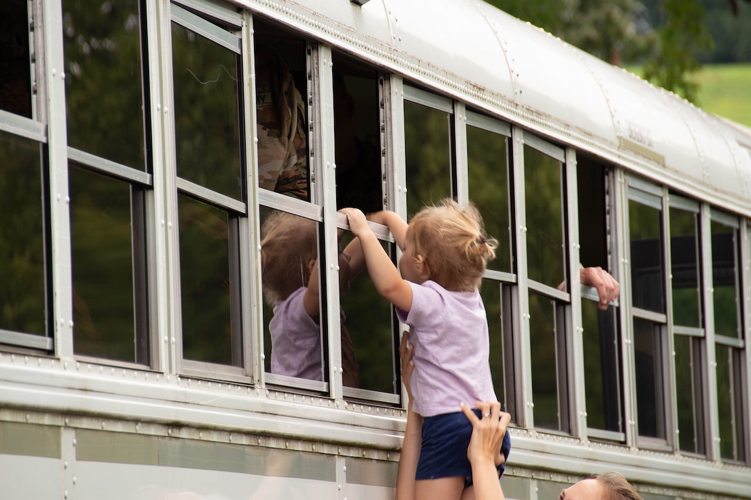 A child is hoisted up and reaches into the window of a military bus.