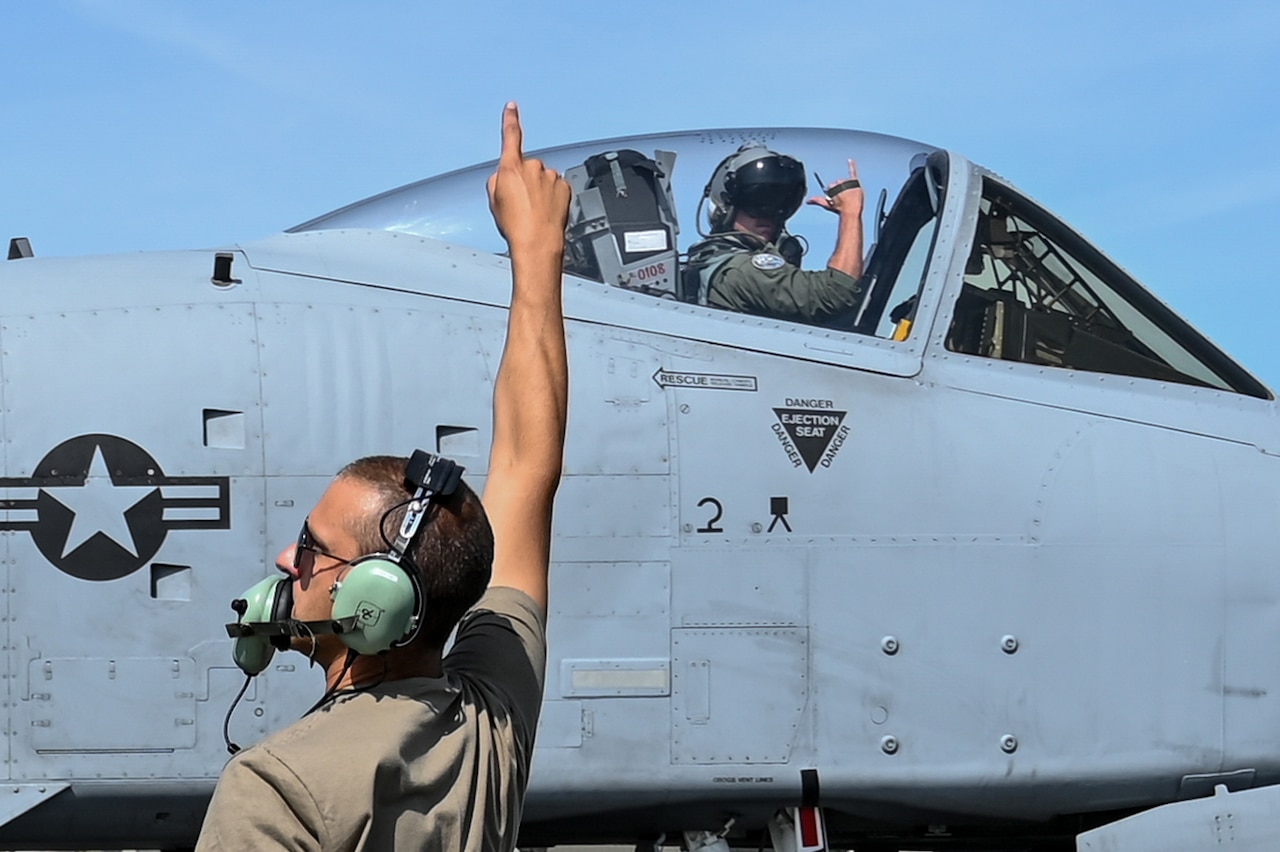 A person standing on the ground signals to a pilot to takeoff.