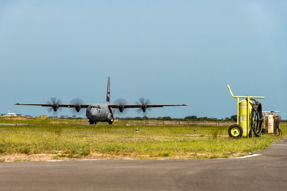A military plane is on the runway and its propellors rotate.