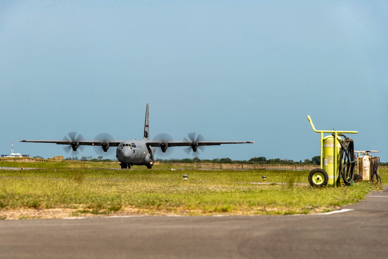 A military plane is on the runway and its propellors rotate.
