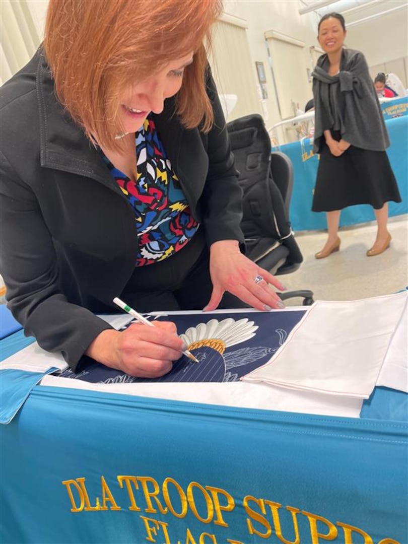 woman signs unfinished flag with eagle embroidery