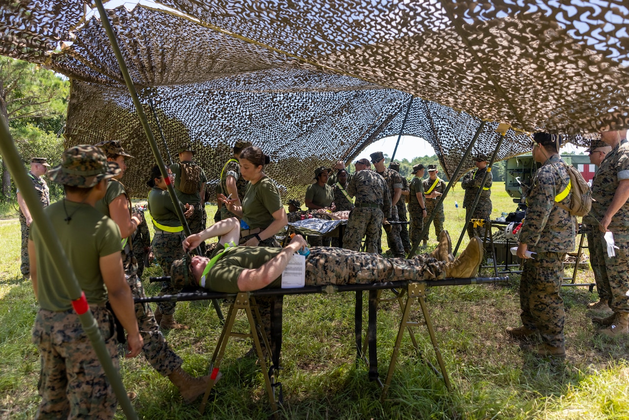 Sailors surround a person on a gurney underneath a tent.