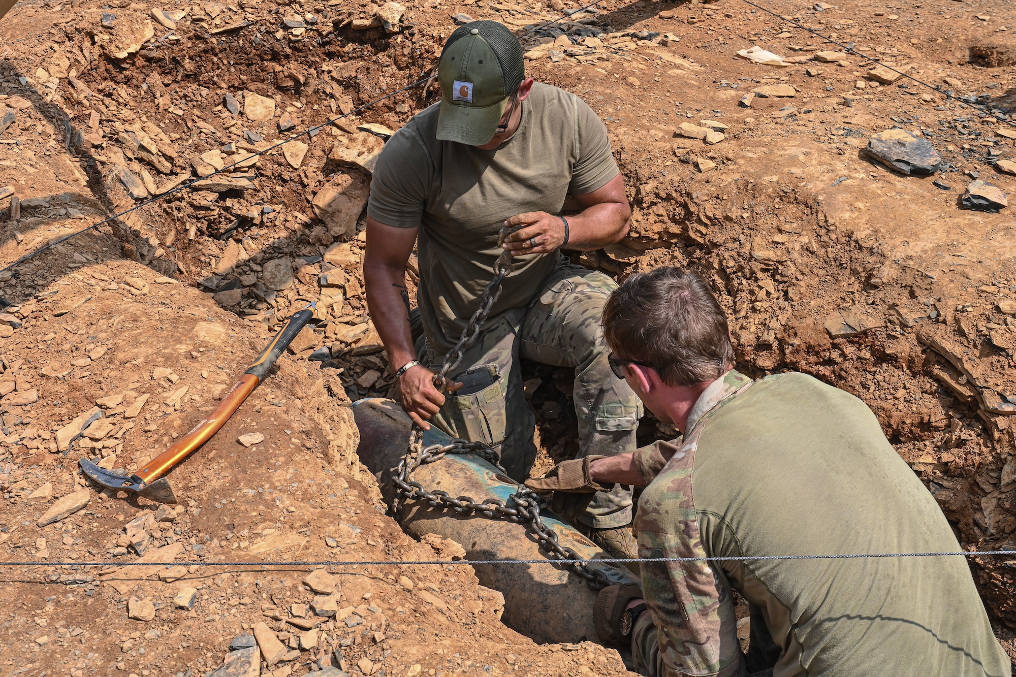 men in uniform wrap a chain around a simulated bomb shell