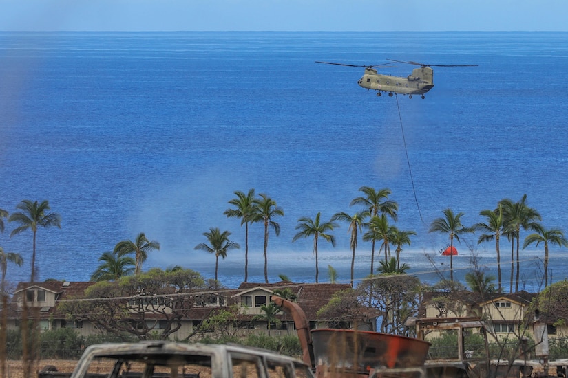 A helicopter scoops water in bucket.