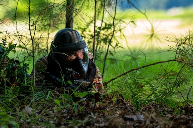 An airman lies on the ground in some bushes during training.