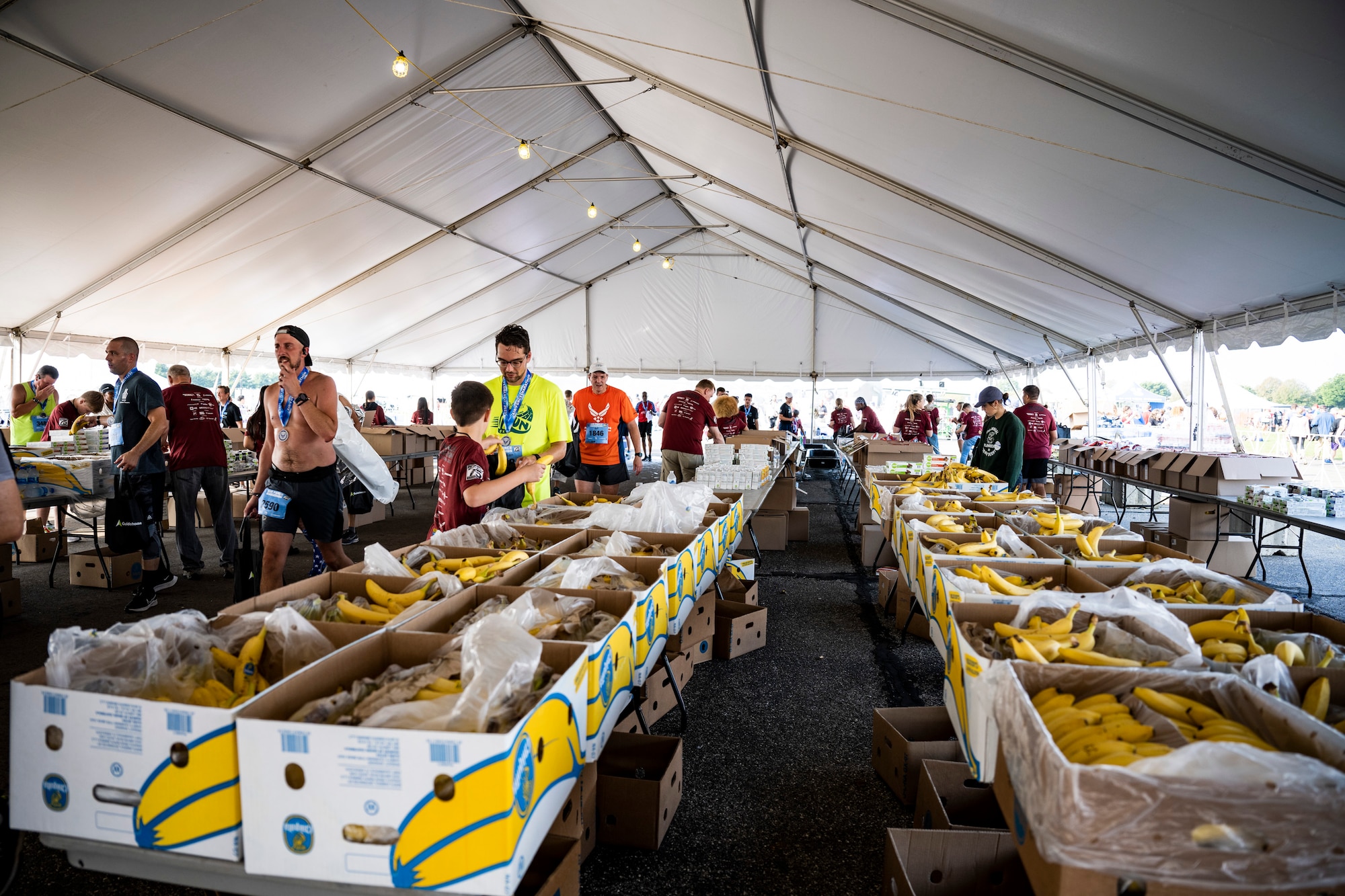Several boxes of bananas on tables where people walk through after crossing the finish line.