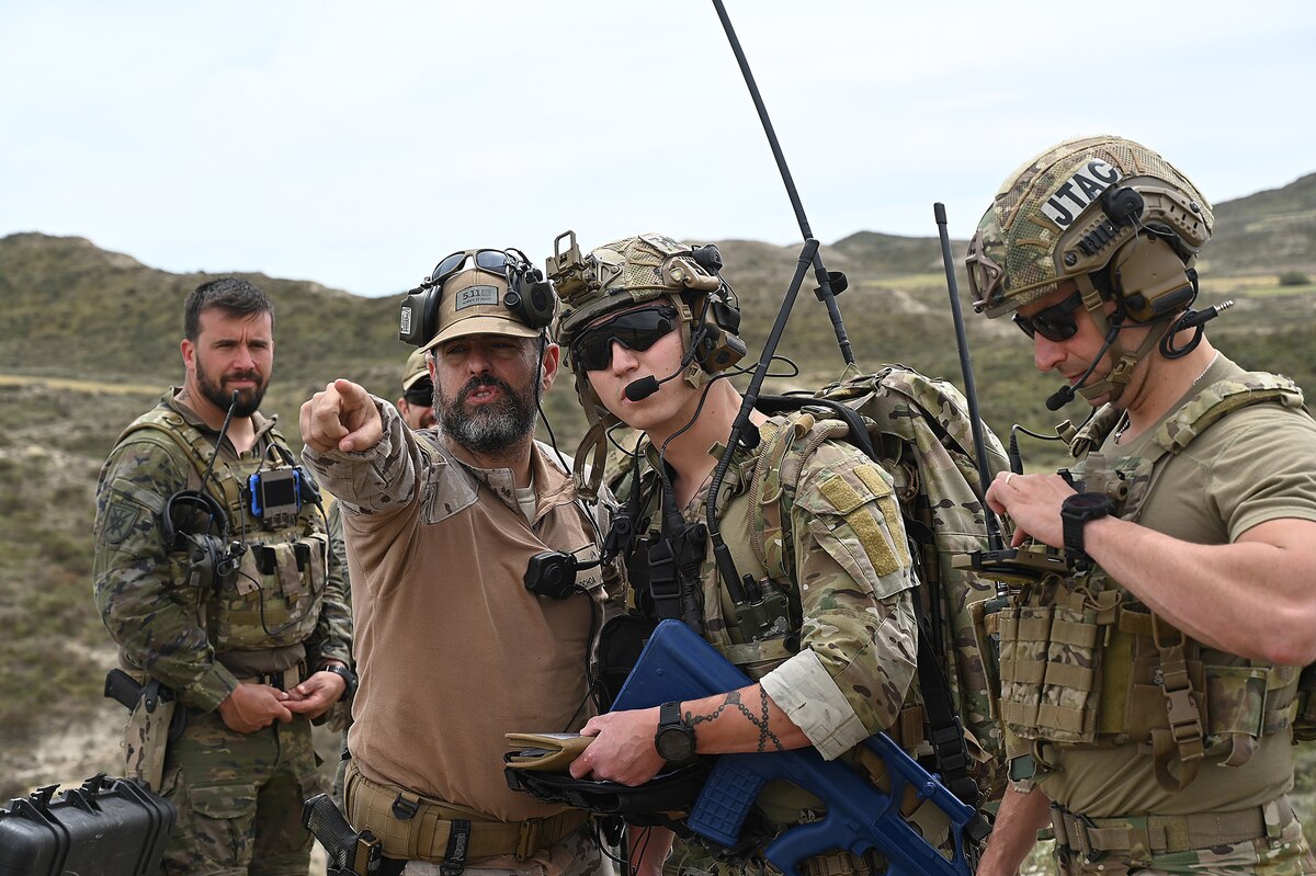 A person points while a uniformed service member looks and others stand nearby.