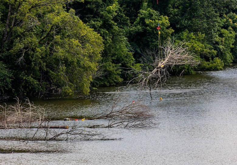 A helicopter lifting trees and concrete blocks to place them in a water basin on the Ohio River.