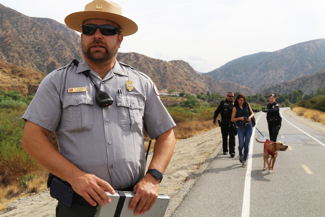 U.S. Army Corps of Engineers Los Angeles District Park Ranger Nick Figueroa assesses the situation, while two law enforcement officers with the Azusa Police Department escort an unhoused individual and her pet for evacuation out of the riverbed near the Santa Fe Dam to a hotel in Azusa, California. Multiple law enforcement agencies, including the LA County Sheriff’s Department’s Homeless Outreach Service’s Team, Azusa and Irwindale police departments; the U.S. Army Corps of Engineers Los Angeles District’s Operations Division; and the Los Angeles Homeless Services Authority collaborated on efforts to evacuate homeless individuals near the dam to safety prior to the impending tropical storm Hurricane Hilary.