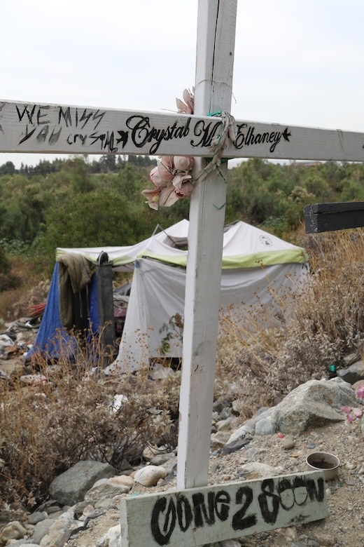 A tent used for shelter shadows the cross of a memorial to a loved one at a homeless encampment in the riverbed near the Santa Fe Dam Aug. 19 in Azusa, California. The cross is a somber reminder about the plight and dangers faced by the area’s homeless population living in Southern California.