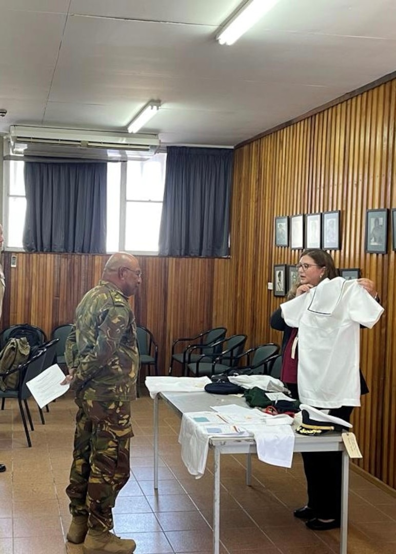 woman holds up white uniform shirt to man in uniform