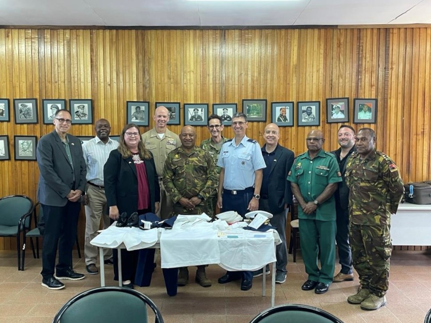 military and civilian men and women pose behind table of uniforms