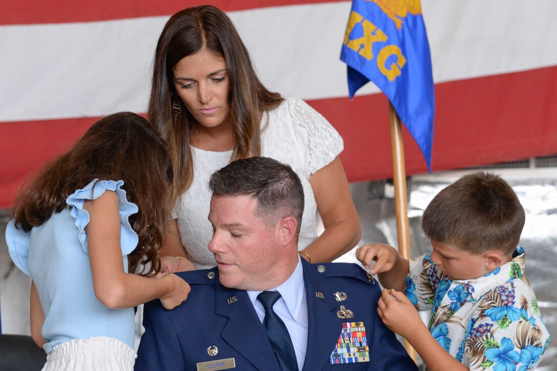 Members of an officer's family pin a new rank on his uniform.