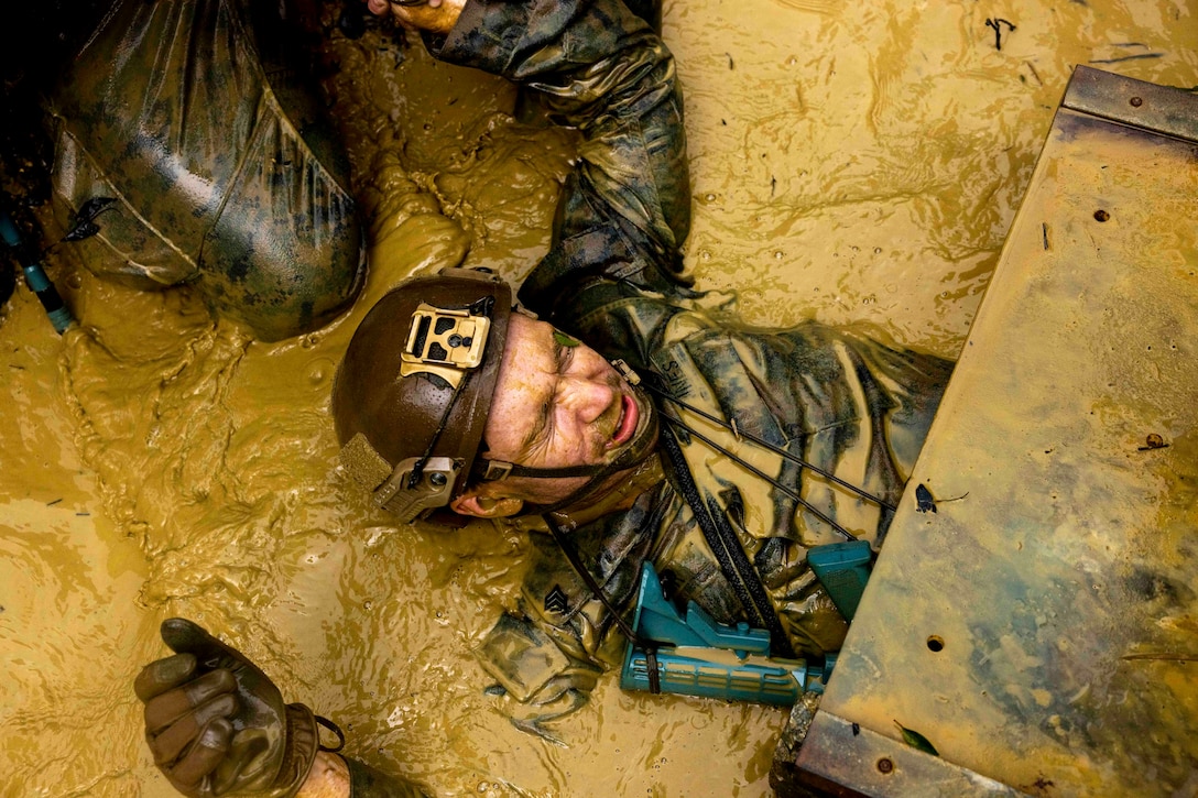 A Marine moves on his back through muddy water.