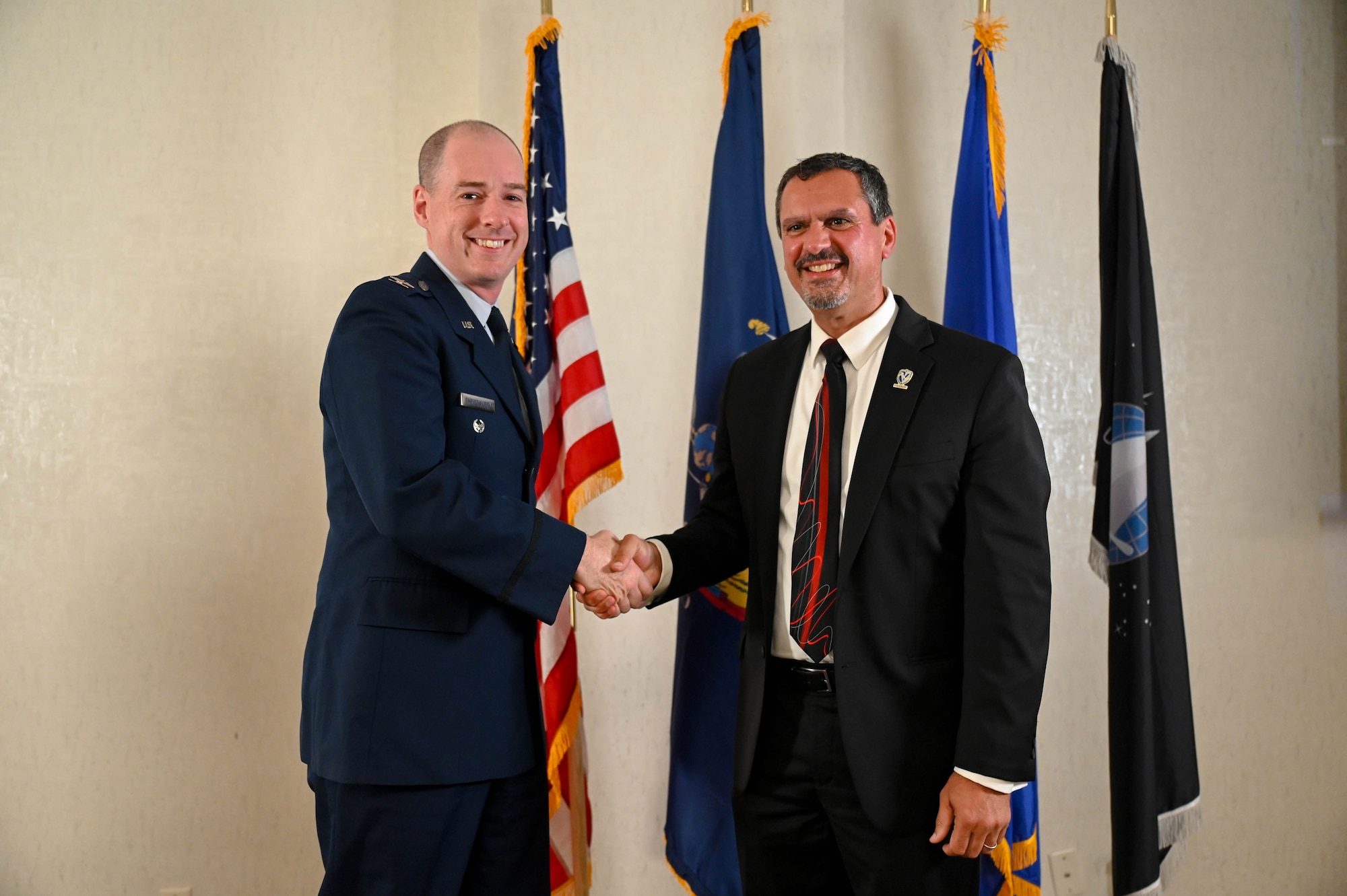 U.S. Air Force Col. John Christianson, 350th Spectrum Warfare Wing deputy commander, left, shakes hands with Chester Maciag, director for cyber and technology research at the Office of the Secretary of Defense for Research and Engineering, right, during the Virtual Institutes for Cyber and Electromagnetic Spectrum Research and Employ (VICEROY) MAVEN graduation ceremony, Utica, New York, Aug. 4, 2023. The wing hosted seven interns this past summer that worked on mission sets such as integrating AI to speed up aircraft reprogramming, building threat representative test models for bombers and F-35s, improving multi-level data analysis processes using new algorithms and improving missile assessment in large force exercises. (U.S. Air Force photo by Capt. Benjamin Aronson)