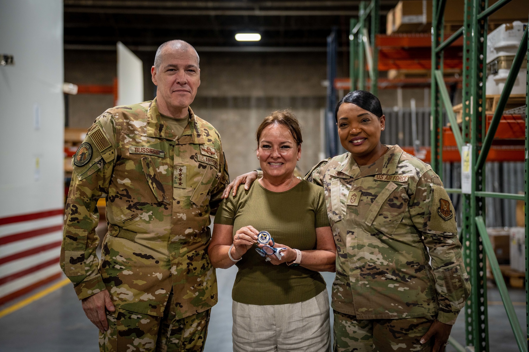 Woman poses with her challenge coin for a group photo with man and woman.