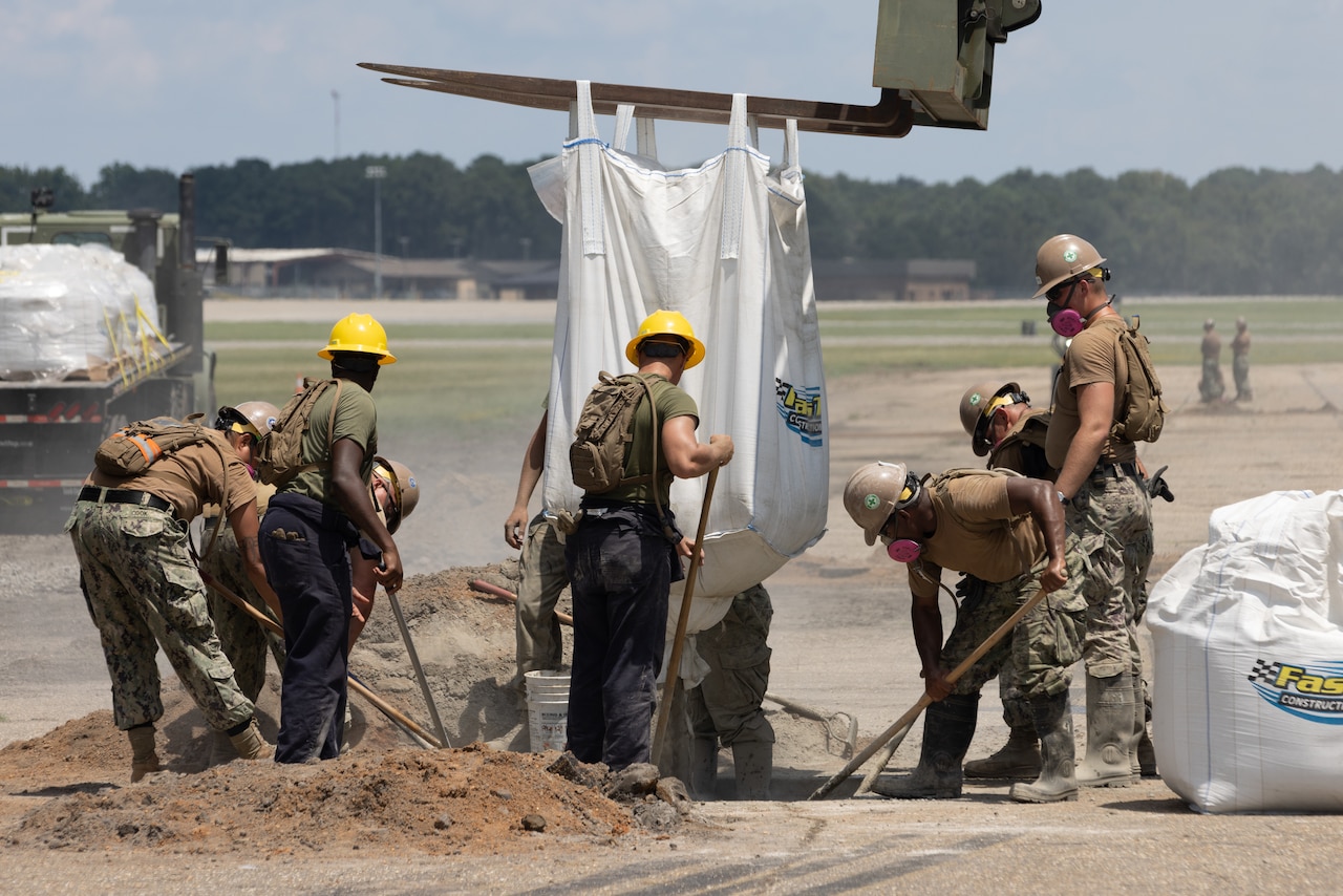 Marines and sailors fill a crater using shovels and construction equipment.
