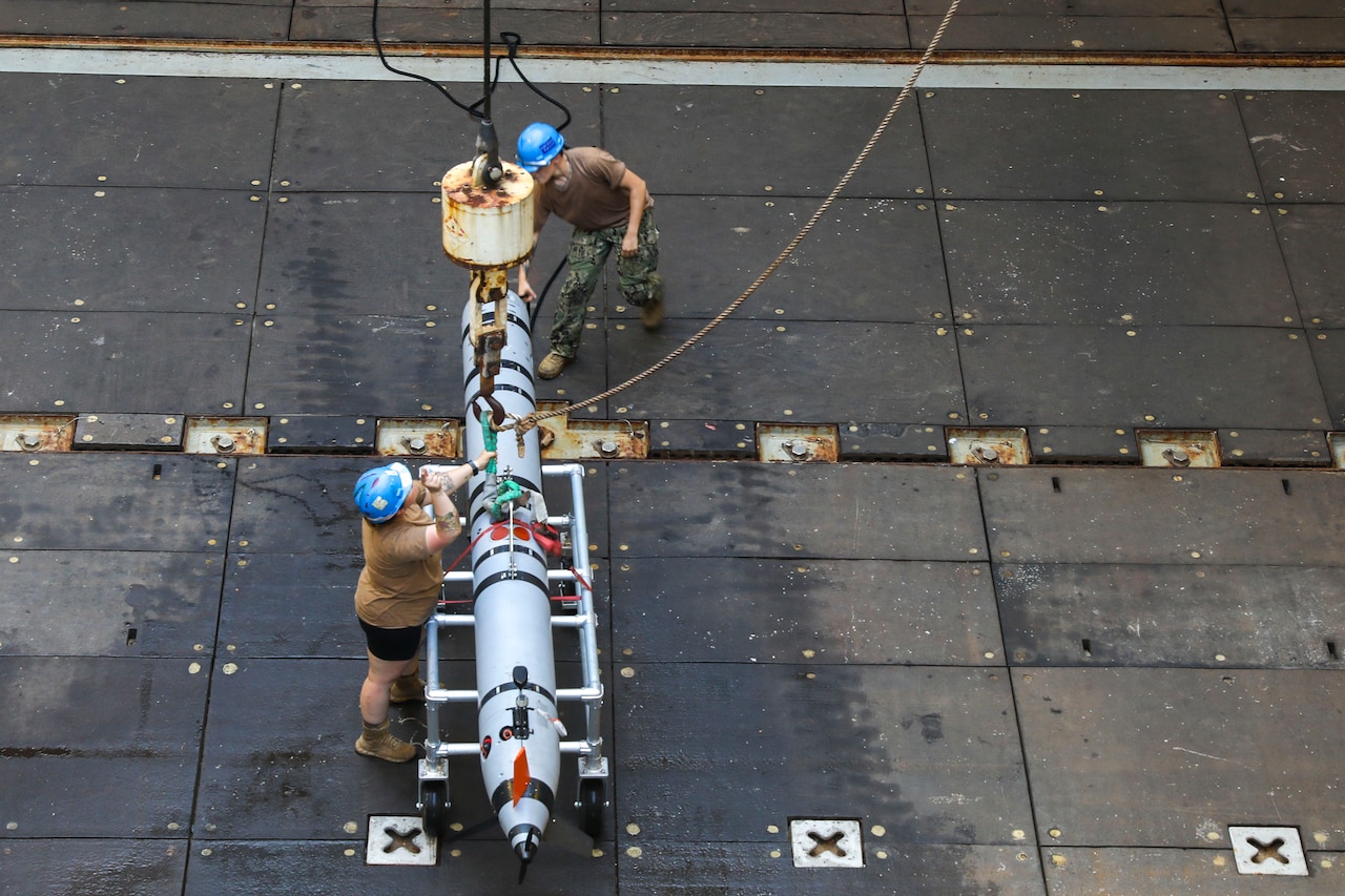 Two sailors prepare to secure an unmanned underwater vehicle to a rope.