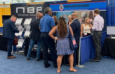 Men and women in business attire stand around a booth with a sign that says Defense Logistics Agency.