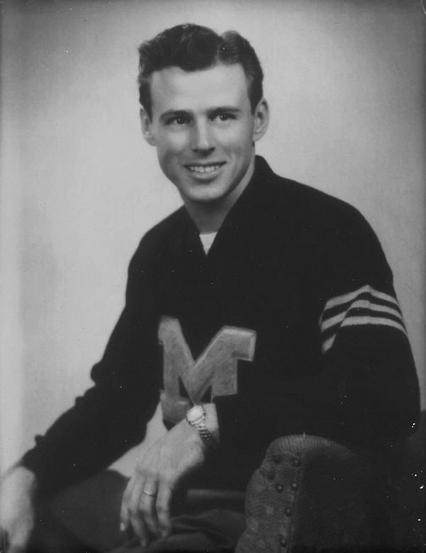 A person man in a varsity letter sweater poses for a black and white photo.