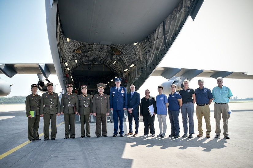 A group poses for a photo near the cargo section of an airplane.