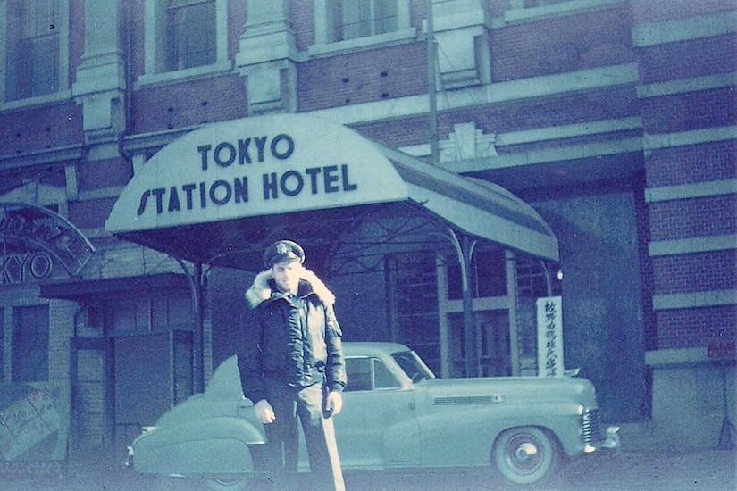 A Korean War-era pilot poses for photo in front of a hotel.