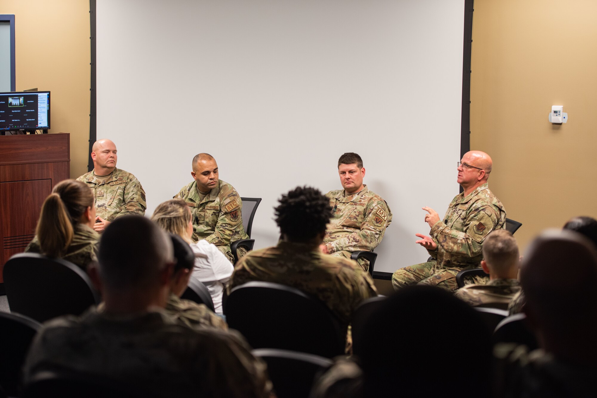 Four chiefs sit in front of multiple Airmen