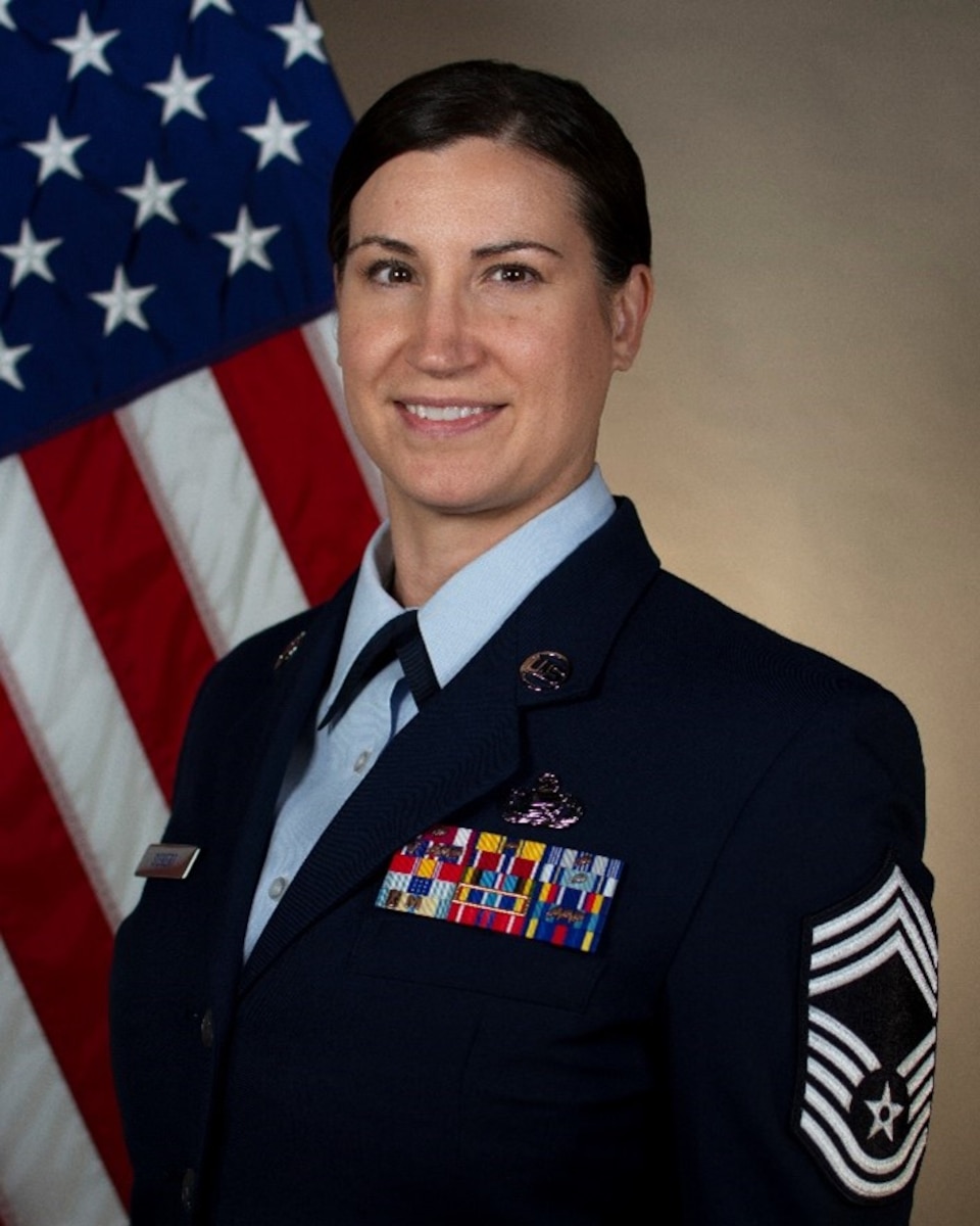 Service member smiles for official portrait in front of US flag wearing their service dress blues