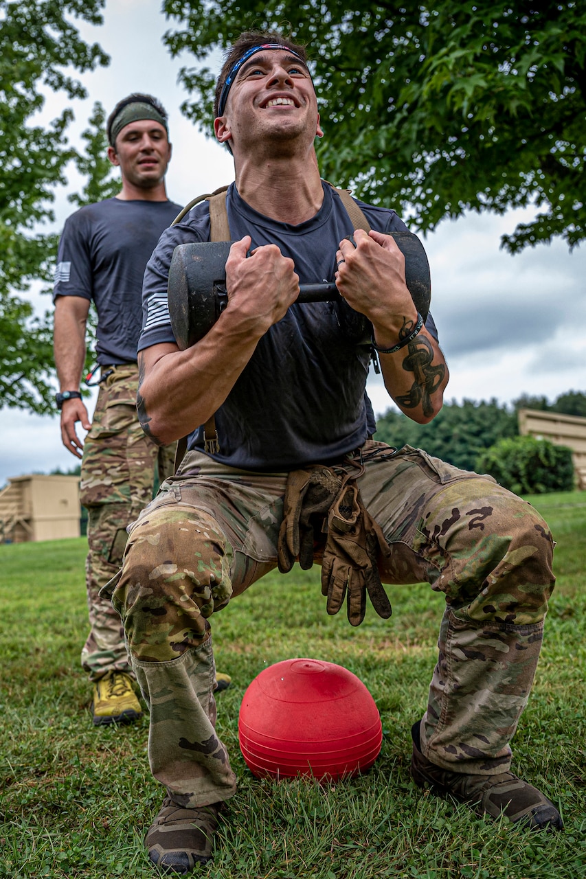 A guardsman squats while holding a dumbbell as a fellow service member watches.
