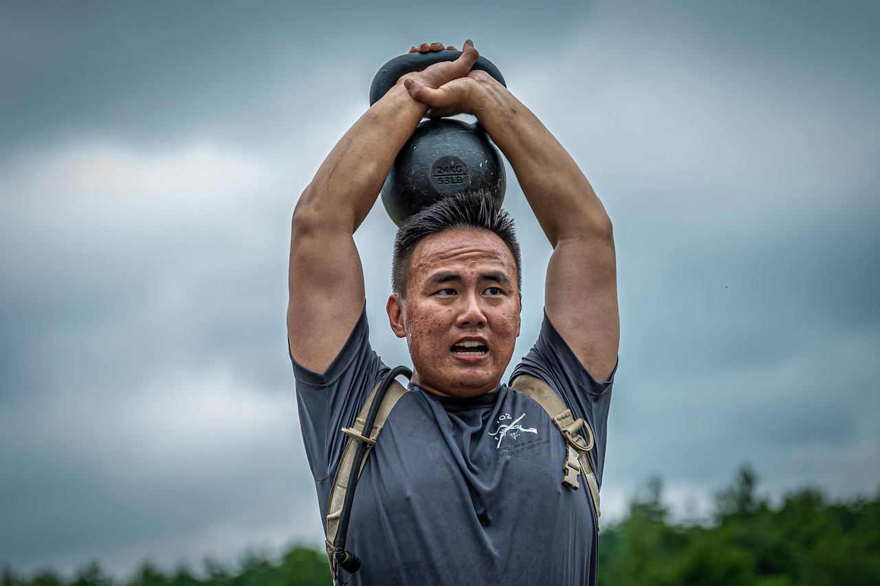 A soldier holds a kettle ball over his head.