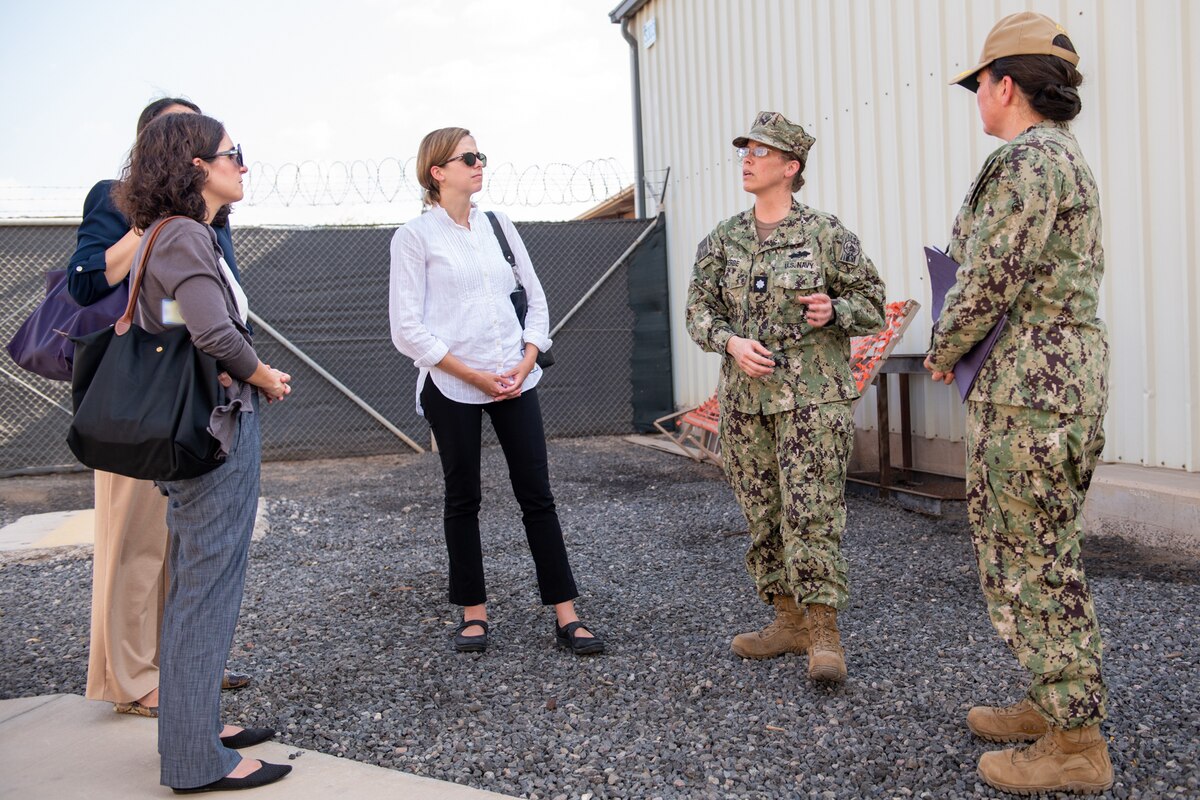Women in civilian attire gather with two navy officers in uniform outside of a facility on a military installation.
