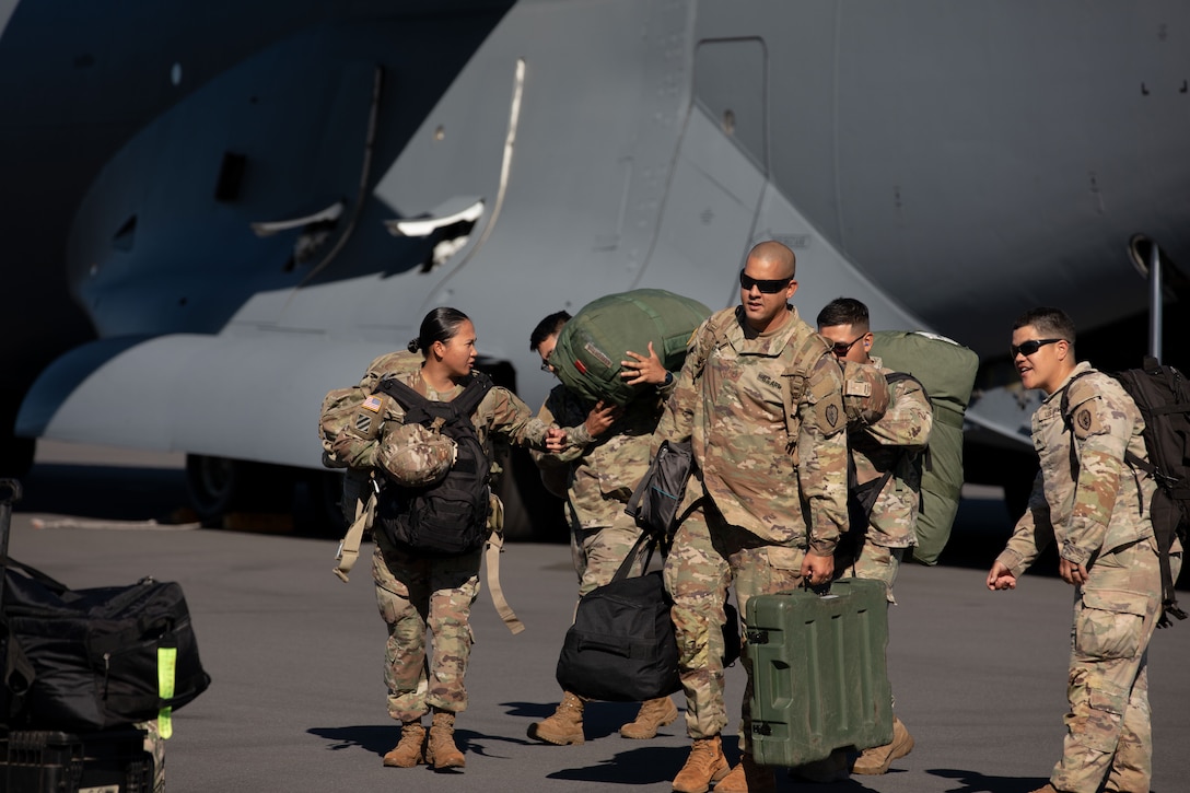 Service members carrying suitcases and bags get off a plane at an airport.