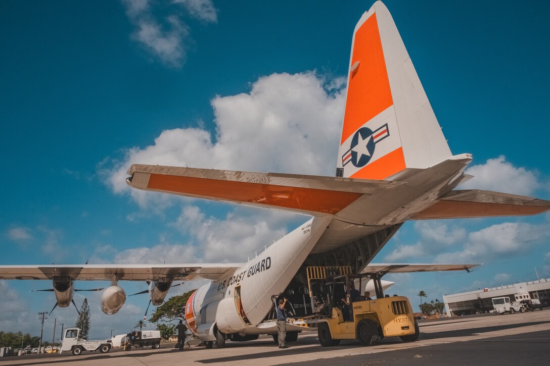 A Coast Guard aircraft is loaded with supplies on the tarmac of an air station.