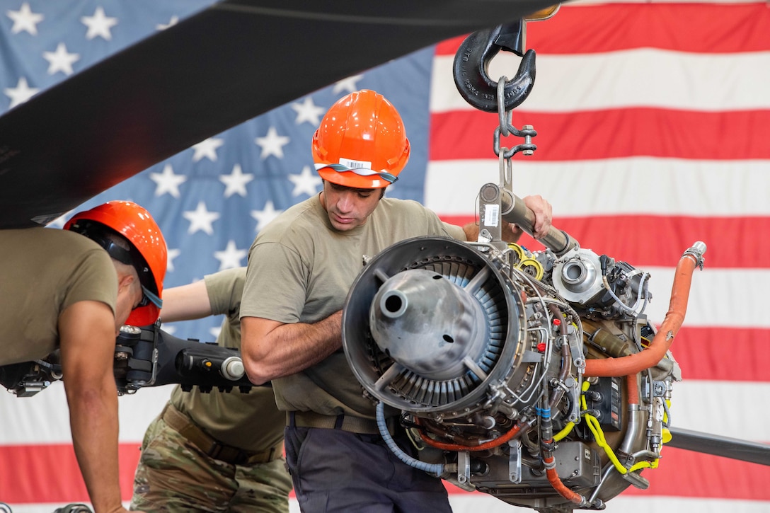 Two airmen replace a helicopter engine.