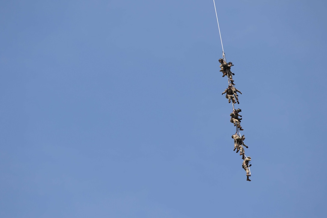 A group of soldiers hang onto a cable in the air.