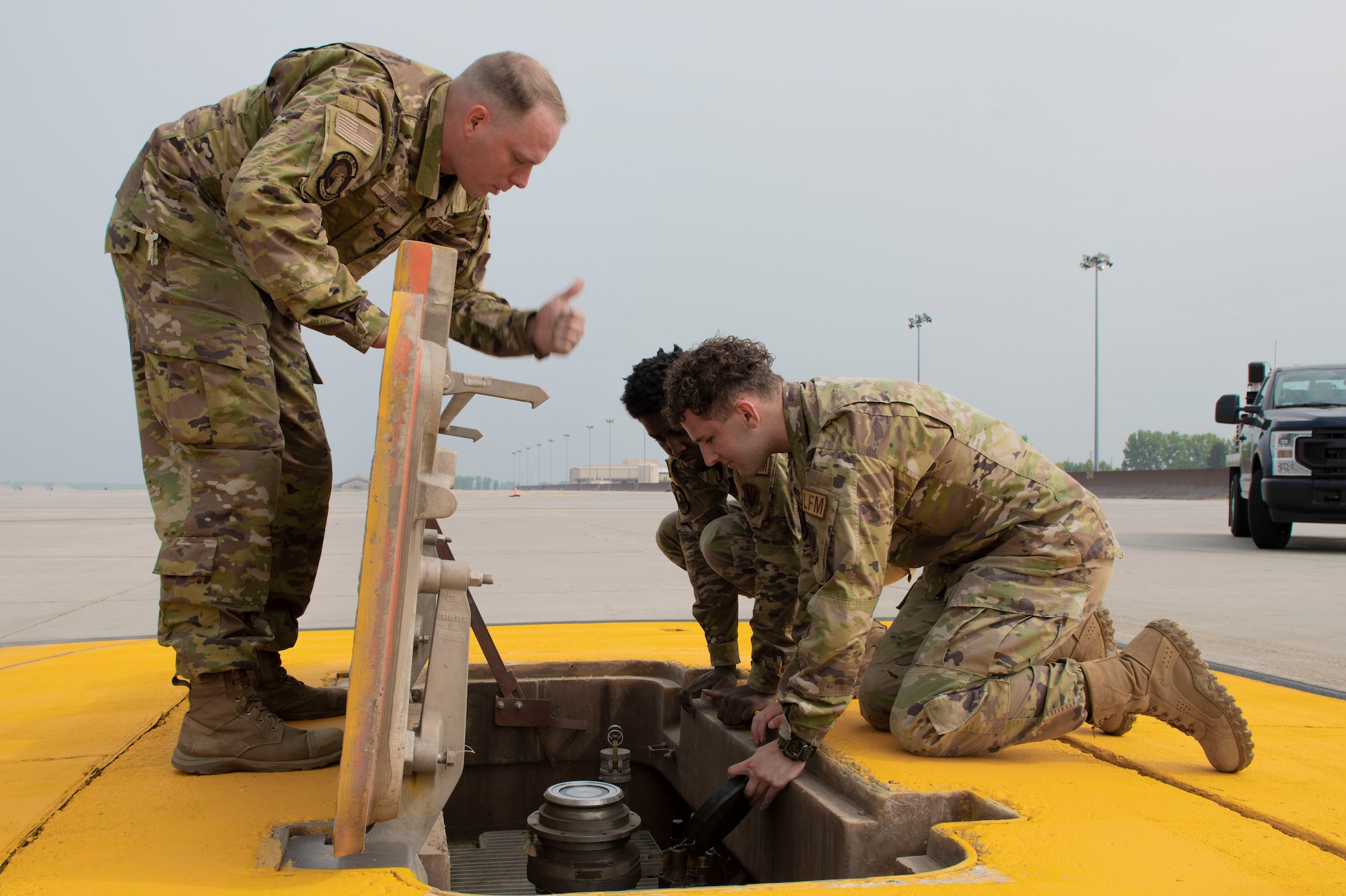 3 Service members look down a hydrant fuel pit.