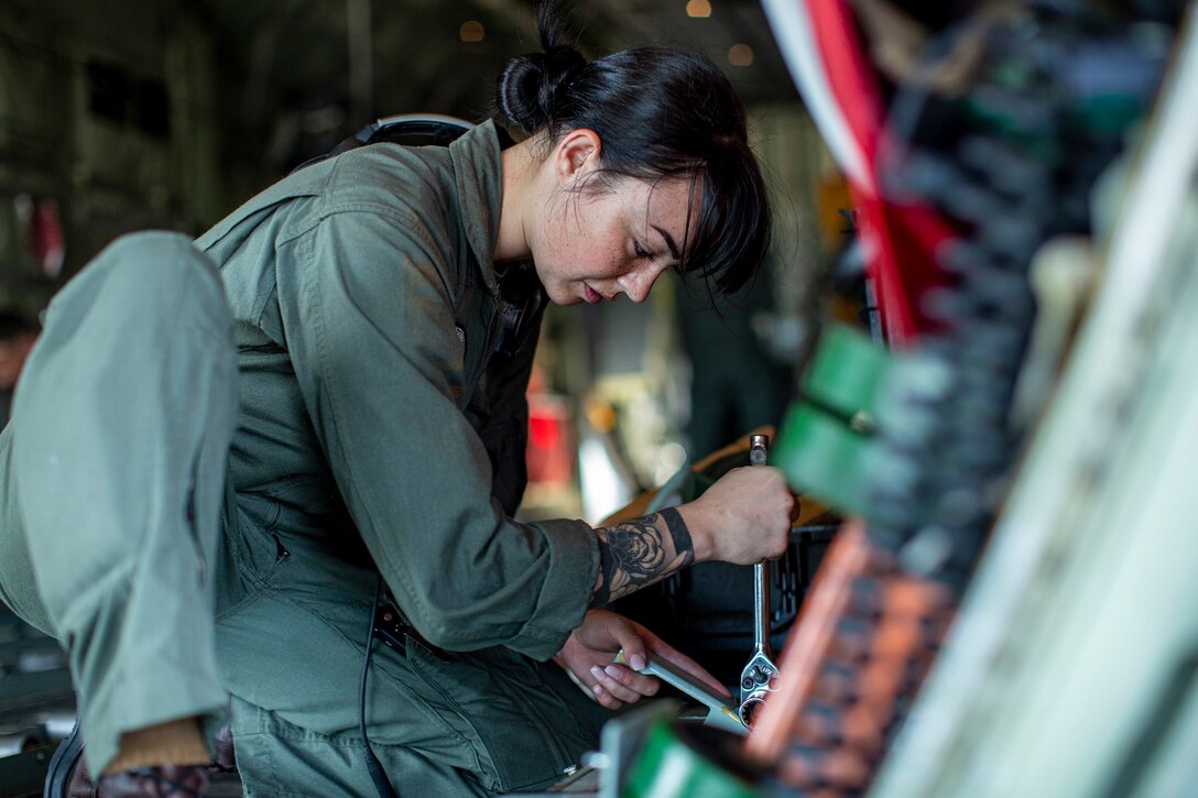 A Marine kneels down to tighten bolts on an aircraft.